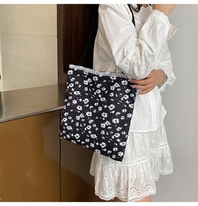 Close-up of black floral canvas tote with white daisy print and lace trim on a model