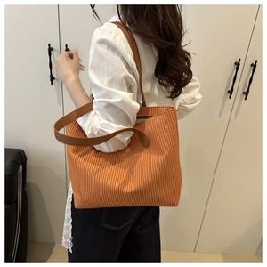 Detail of orange woven tote bag with brown leather straps shown on a female model