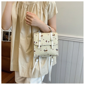 Detailed view of mini cream backpack with cartoon puppy prints and dual buckle flap closure