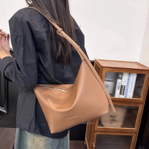 Brown soft leather tote bag with metal zipper detail and adjustable strap on a model