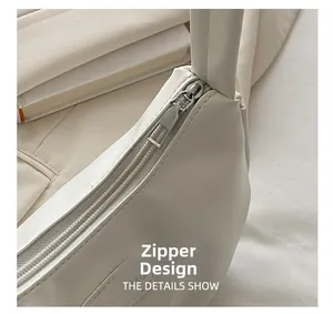 Detailed close-up of the smooth metal zipper and leather texture on a white underarm bag