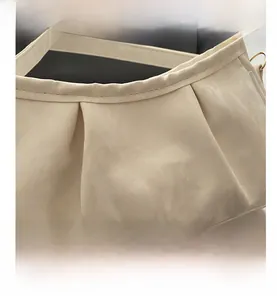 Detail of cream white pleated leather bag with delicate textures and gold-toned metal rings