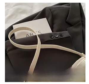 Detail of off-white pleated handbag with shoulder strap on a dark grey blazer jacket