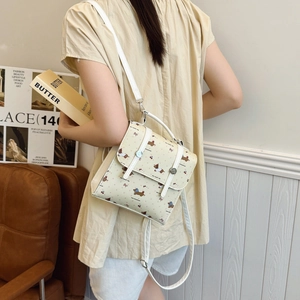 Beige mini backpack with cartoon puppy print shown on model from a back-side angle
