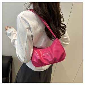 Detail of fuchsia pleated baguette bag with metal logo on model shoulder