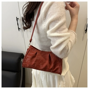 Close-up of a retro reddish-brown pleated cloud bag worn by a model in a home setting
