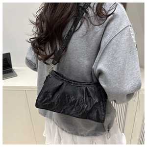 Detail of black pleated shoulder bag with glossy finish and delicate gold hardware