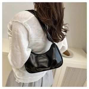 Model wearing a black glossy underarm bag with pleated design and metal logo detail