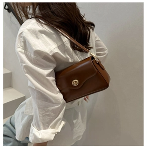 Detail of a brown leather crossbody bag featuring a golden circular twist lock buckle