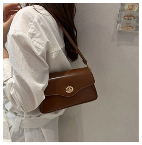 Detail of brown leather shoulder bag with golden metallic swivel lock and fine stitching