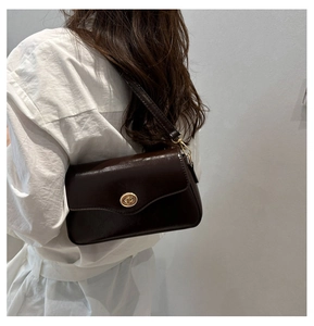 Detail of a dark brown crossbody bag with a gold twist lock on a white shirt