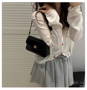 Detail of minimalist black crossbody bag featuring a golden round twist lock buckle