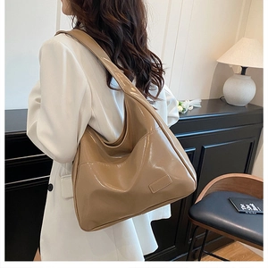 Elegante borsa hobo marrone in pelle verniciata lucida indossata da una modella in blazer bianco