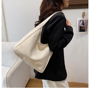 Dettaglio di una grande borsa hobo in vernice crema lucida indossata a spalla per ufficio