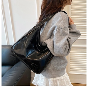 Model wearing a large black glossy patent leather hobo tote bag with a modern design