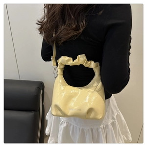 Detail of light yellow ruched cloud bag showing glossy leather texture and logo lettering