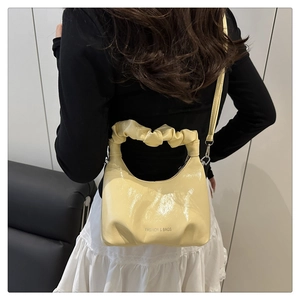 Detail of butter yellow pleated handbag with glossy finish and cloud-shaped handle