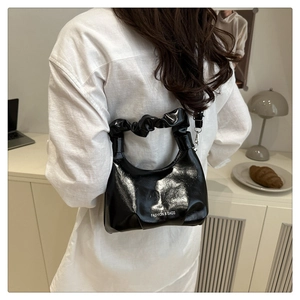 Detail of a shiny black pleated handle handbag with Fashion & Bags lettering on a model