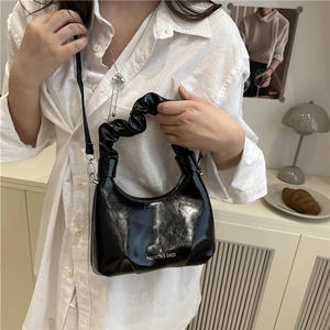 Fashionable black glossy ruched handbag with white lettering and chain strap in daily use