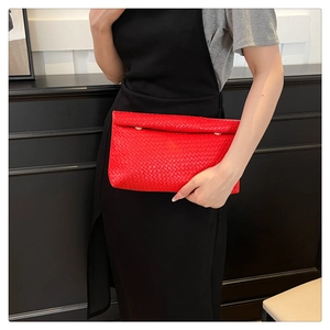 Detail of red woven leather clutch with gold clasp shown against black dress