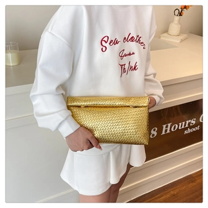 Detail of a gold woven texture clutch bag with flap closure held by a model in casual attire