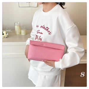 Detail of pink woven leather envelope clutch held against a white lifestyle background