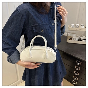 Detailed view of a white glossy baguette bag featuring top handles and long shoulder strap