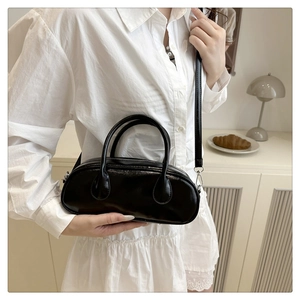 Close-up of a glossy black Boston bag on a minimalist cabinet with a stylish lamp