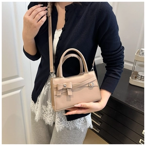Detail showing the elegant bow decoration and metal buckle on the beige leather handbag