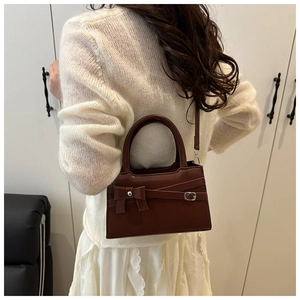Detail of dark brown mini square bag with decorative bow and metal buckle on white sweater