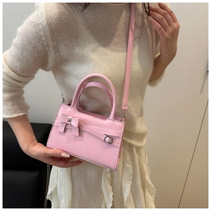 Pink PU leather crossbody bag featuring a bow detail worn by a model in a casual outfit