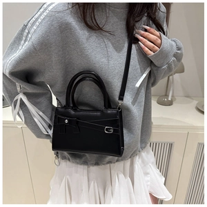 Close-up of black handbag featuring a decorative bow and adjustable crossbody strap