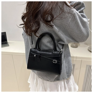 Detail of black leather crossbody bag with decorative bow and metal buckle on the front