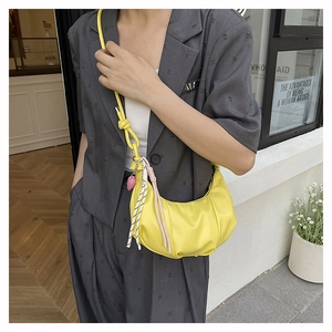 Detail of a yellow crescent bag with knotted strap and woven pendant on a grey blazer
