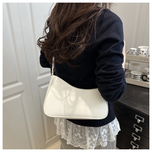 Rear view of a white leather underarm bag with gold accents on a model's shoulder