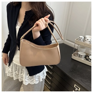 Detailed close-up of a beige faux leather underarm bag held by a model in a home setting