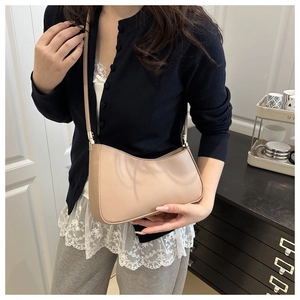 Sac sous l'aisselle croissant beige porté à l'épaule dans un décor minimaliste chic