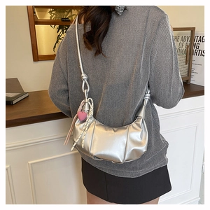 Silver pleated half moon bag with pink heart charm shown on a shoulder in an indoor setting