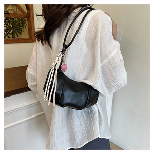 Detail of black leather crescent bag with pink heart charm and striped tassel accessory