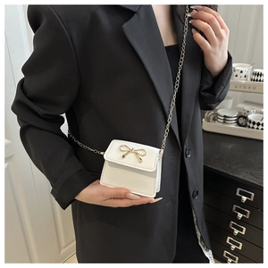 Close-up of mini white leather crossbody bag with gold bow clasp on a model's black suit