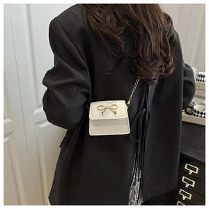 Mini cream saddle bag with golden bow clasp shown as an elegant shoulder accessory
