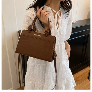Detail of dark brown crocodile-pattern handbag with knot handle and golden fashion text