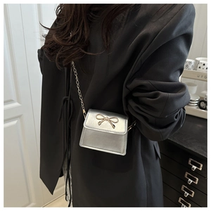 Close-up of a silver mini saddle bag with a golden bow buckle and delicate chain strap