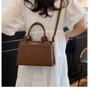Detail view of brown crocodile texture handbag with gold fashion lettering logo
