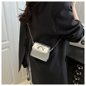 Close-up of mini silver square crossbody bag with gold bow on a black blazer
