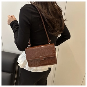 Detail view of dark brown crocodile texture shoulder bag with silver metal lock closure