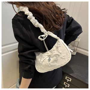Detalle de bolso medialuna blanco con textura floral y colgante de corazón plateado