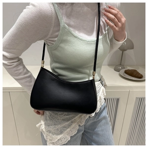 Minimalist black crescent shoulder bag with golden hardware shown in a lifestyle setting