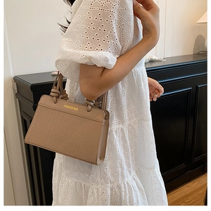 Detail of beige crocodile embossed tote bag with knot handle and gold fashion bag text