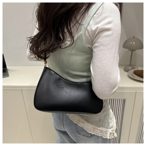 Close-up of minimalist black PU leather hobo bag with gold hardware worn by a model